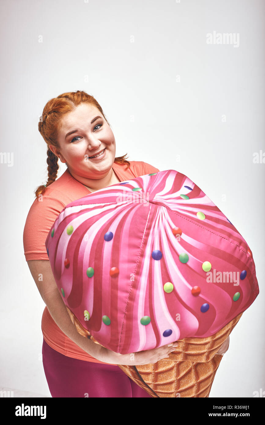 Dai capelli rossi, chubby donna è in possesso di un enorme gelato. Close-up Foto Stock