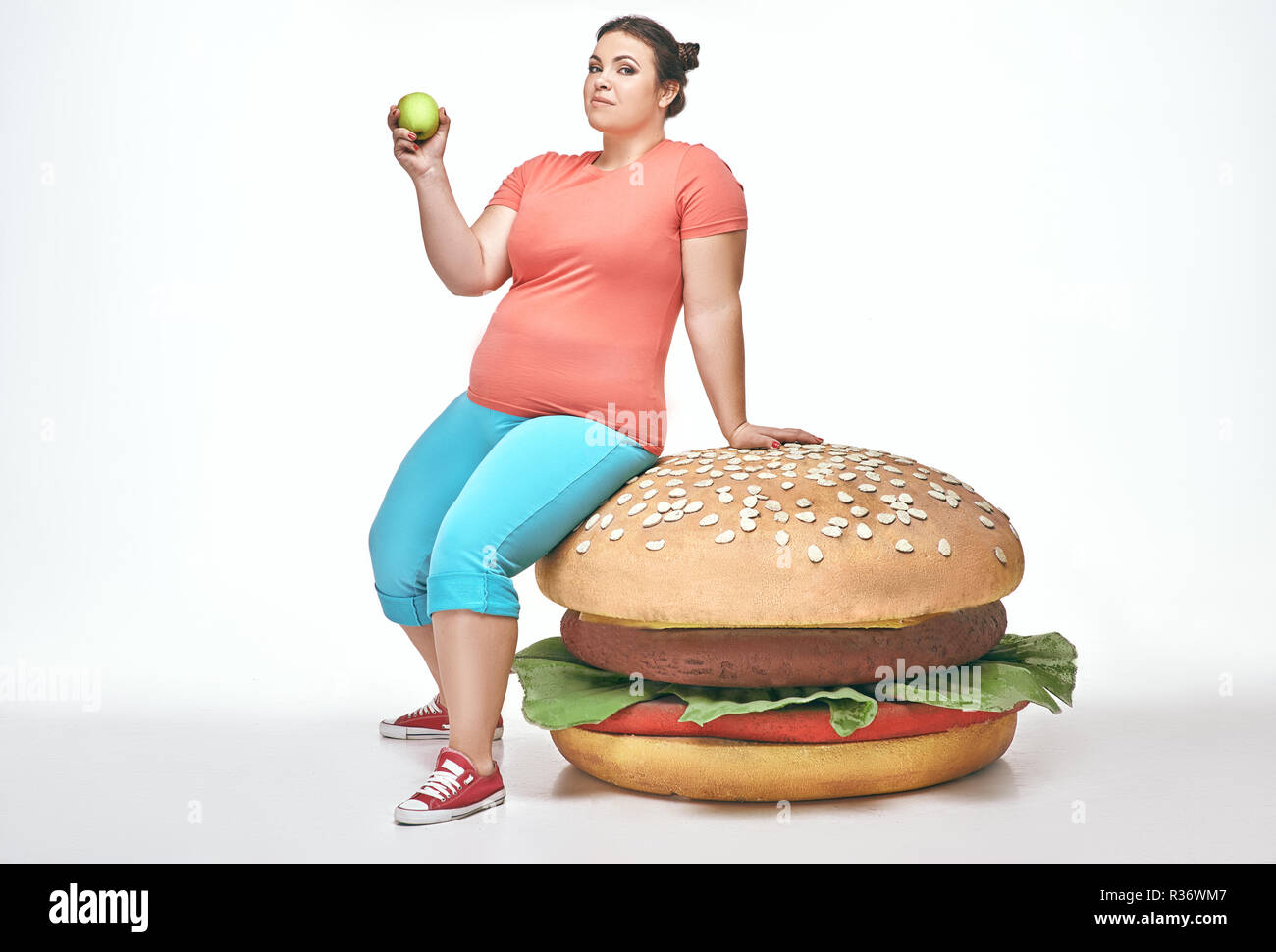 Bruna, divertente, paffuto donna siede su un enorme panino Foto Stock