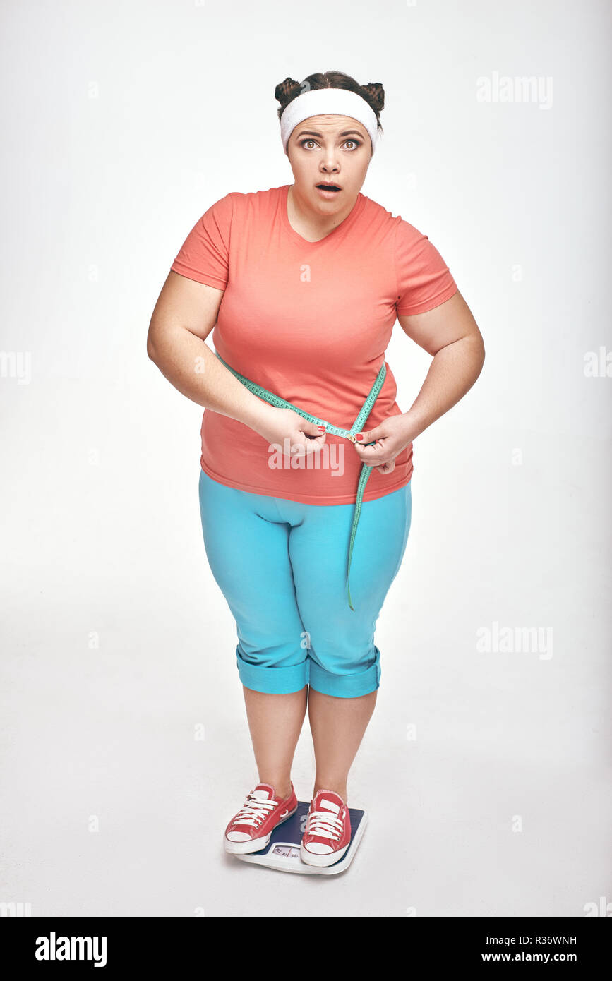 Chubby donna è la misura del suo ventre su sfondo bianco Foto Stock