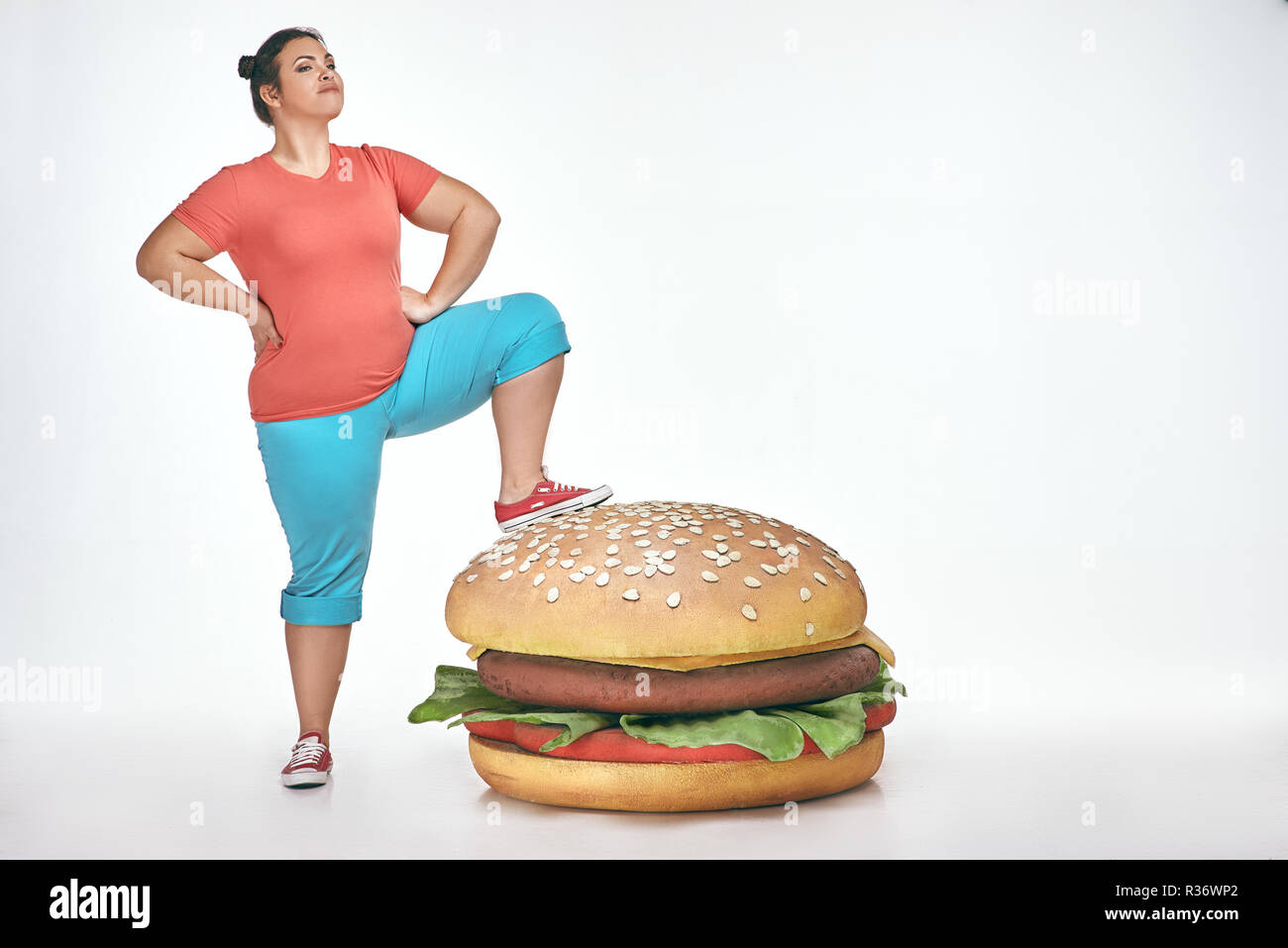 Bruna, divertente, paffuto donna mettere la sua gamba a un enorme panino Foto Stock