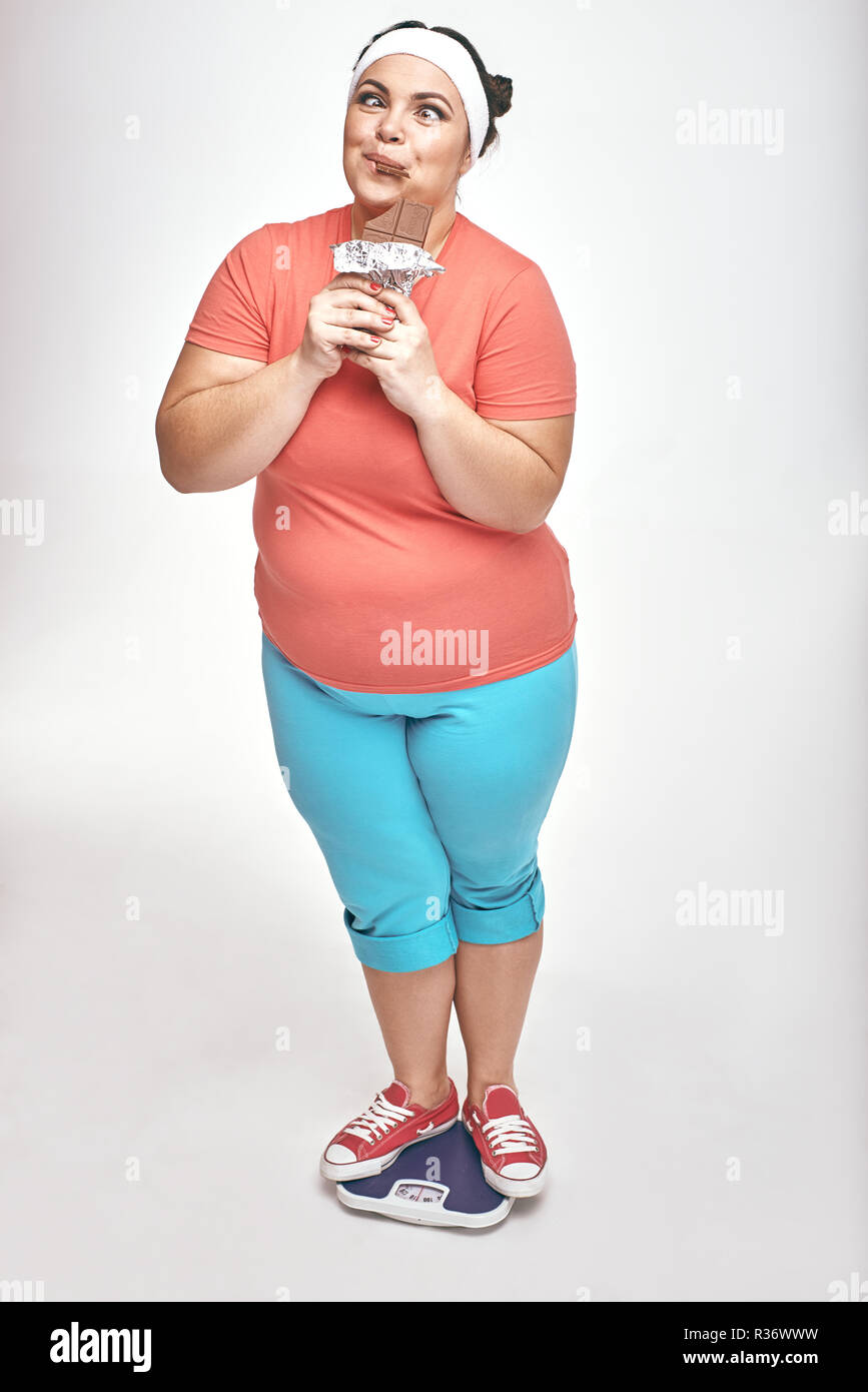 Divertente, chubby donna è mangiare il cioccolato mentre in piedi sulle scale Foto Stock