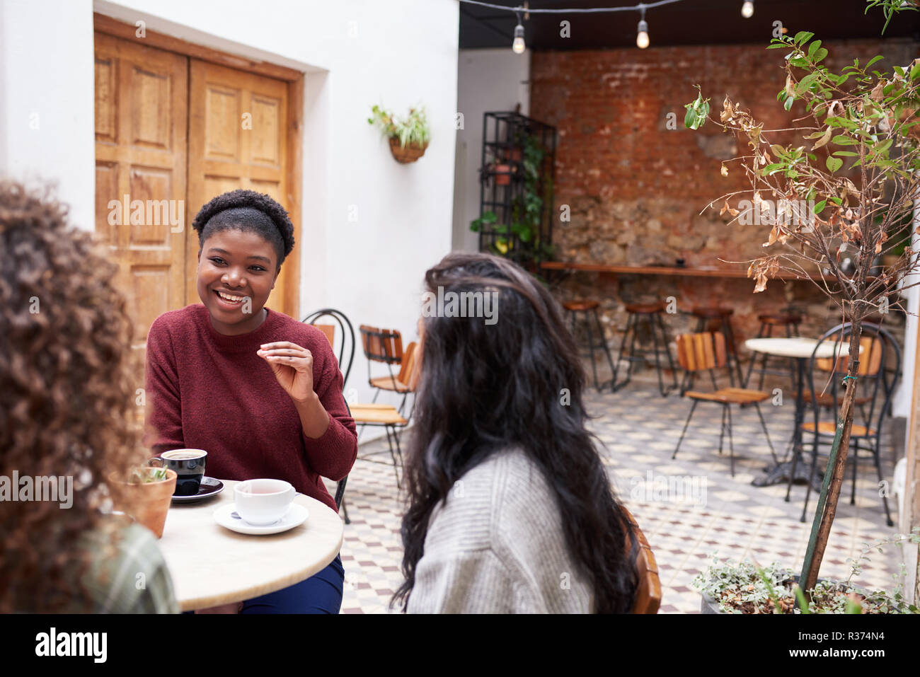 Amici di sesso femminile in chat con un drink in un bar alla moda cortile Foto Stock