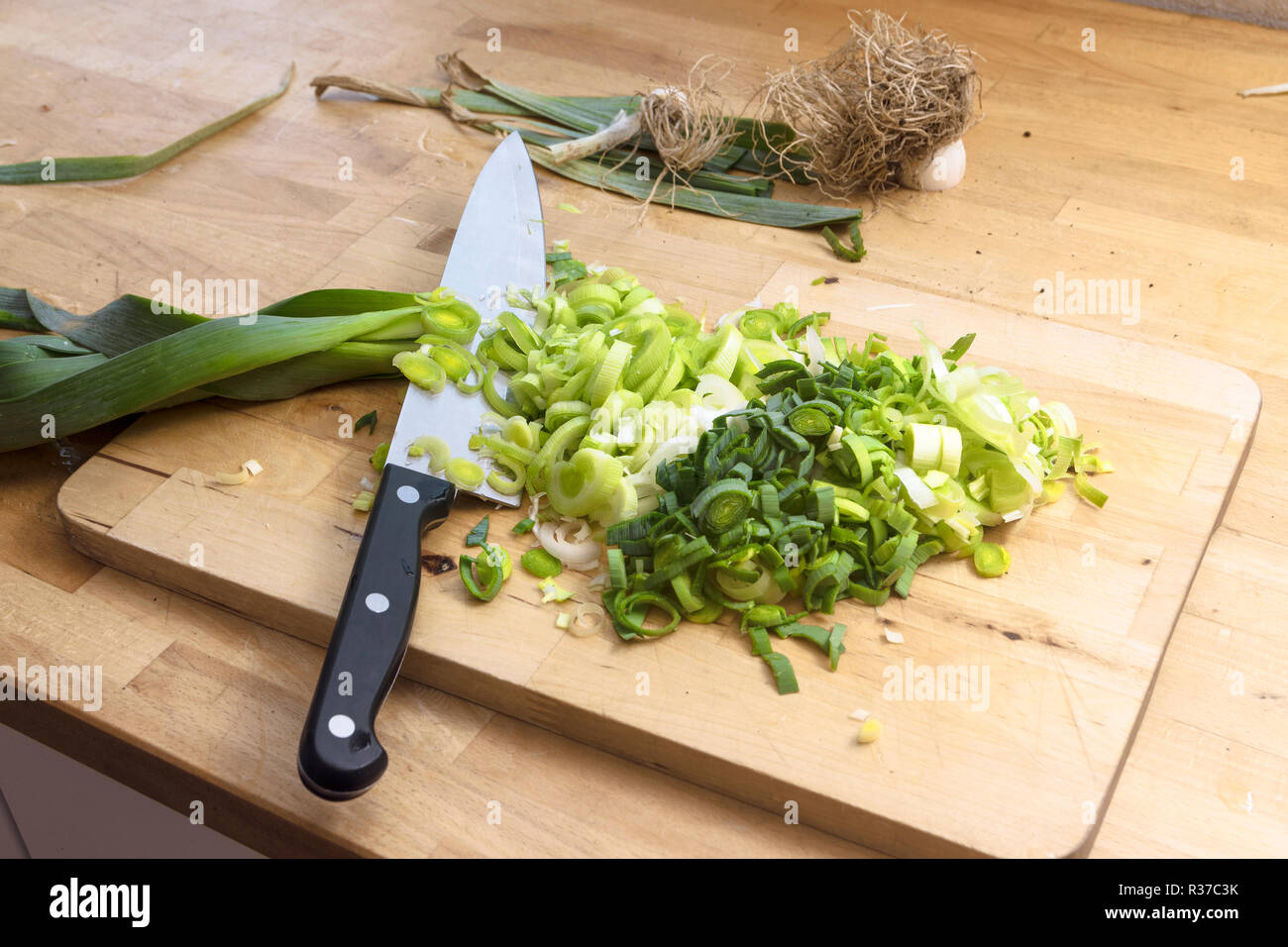 Tagliate a fette il porro e un grosso coltello da cucina in legno piano cucina, concetto di cucina a vista con spazio di copia selezionato, focus, profondità di campo ridotta Foto Stock