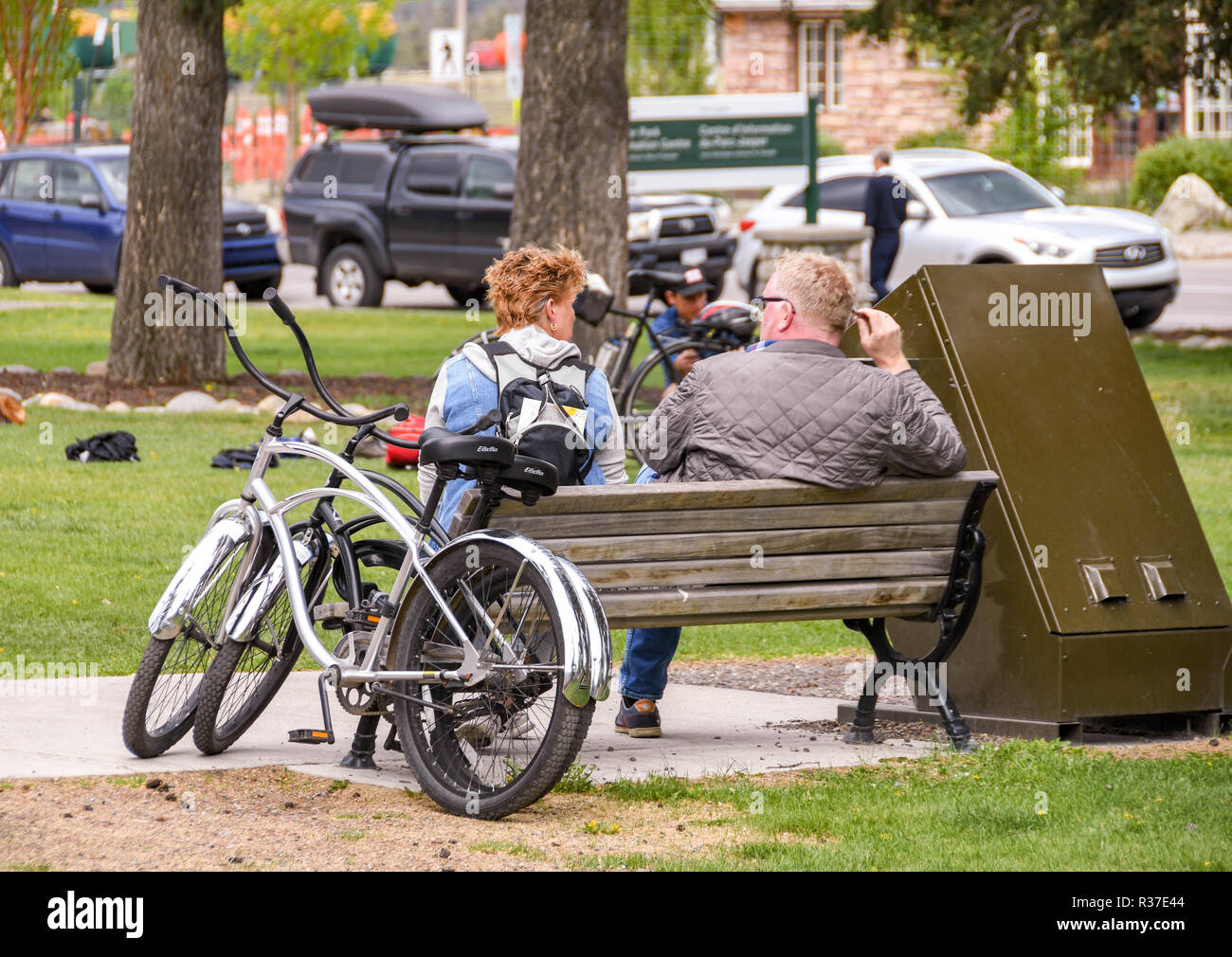 JASPER, AB, Canada - Giugno 2018: Due ciclisti prendendo una pausa seduta su una panchina a parlare in un parco di Jasper, Alberta, Foto Stock