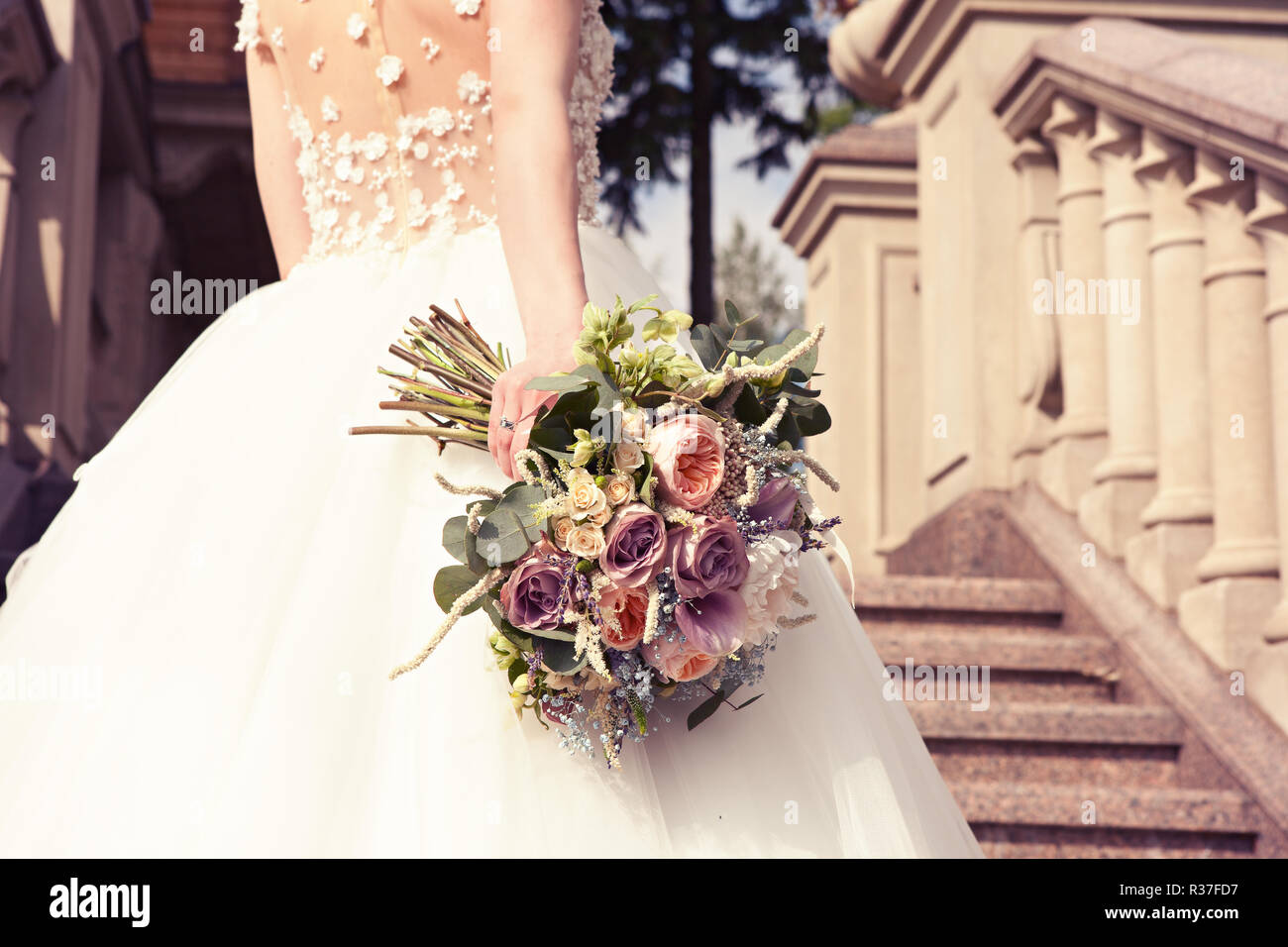 Sposa in un abito bianco con un bel mazzo di nozze su una scalinata di marmo in un vecchio castello. Accessori di nozze. Cerimonia di nozze concetto. Foto Stock