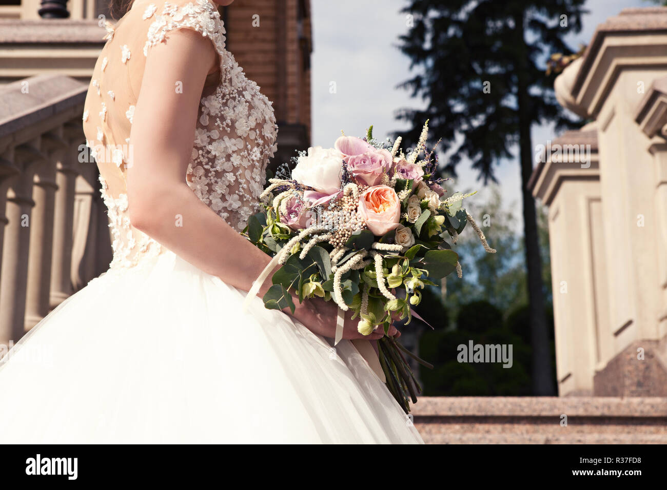 Sposa in un abito bianco con un bel mazzo di nozze su una scalinata di marmo in un vecchio castello. Accessori di nozze. Cerimonia di nozze concetto. Foto Stock