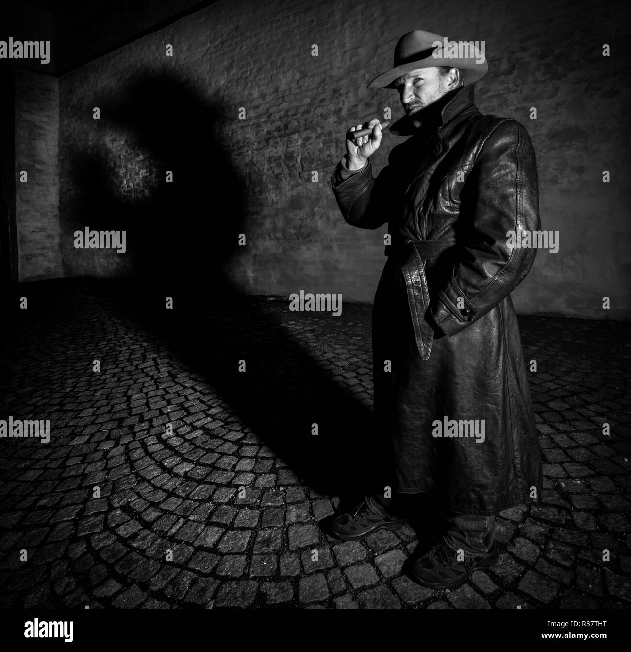 L'uomo con il cappello e il cappotto di pelle fuma sigari, ombra nel retro, night shot, Germania Foto Stock