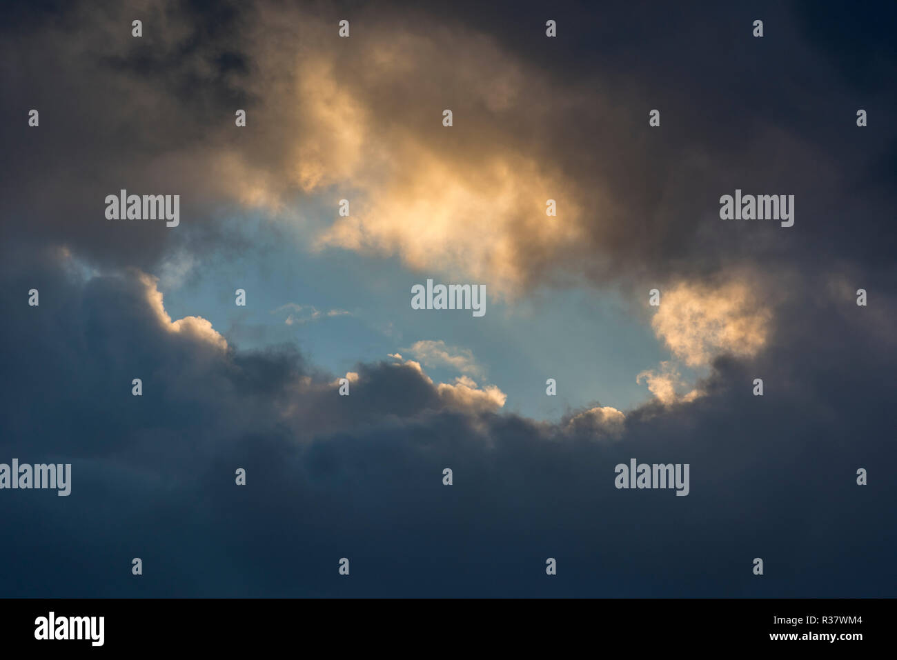 Un foro nella nuvola in un giorno di tempesta con una apertura di cielo blu all'interno tra le nuvole grigio. Foto Stock