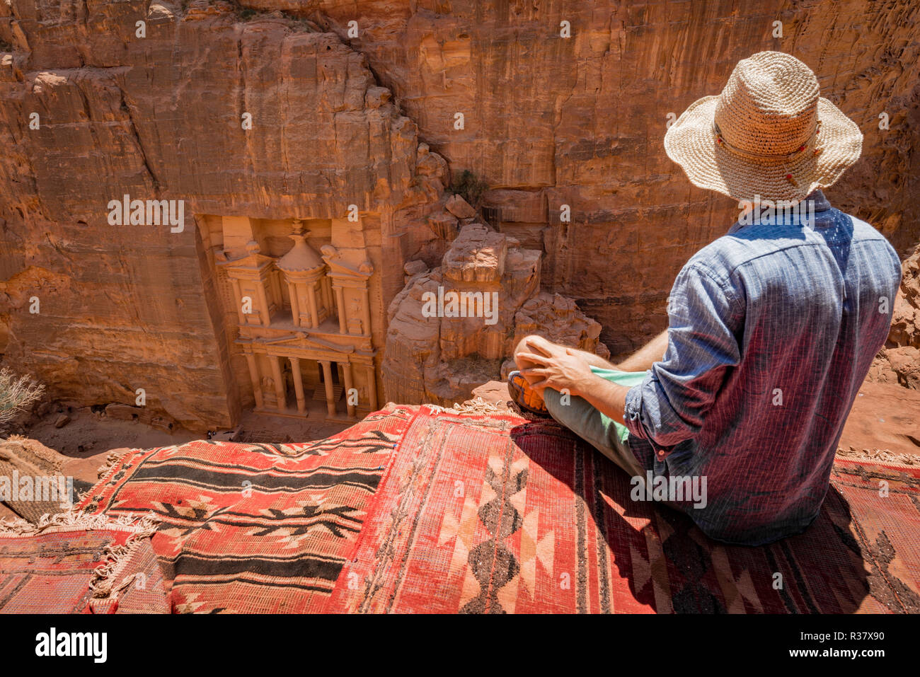 Turistico con cappello per il sole seduti su un tappeto, guardando dal di sopra nella gola Siq, faraone treasure house scavata nella roccia, facciata Foto Stock