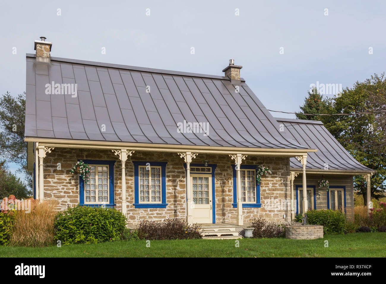 Vecchio 1820 cottage in stile casa fieldstone facciata con rivestimento blu e marrone e giunzione permanente di lamiera tettuccio più log impilati Foto Stock