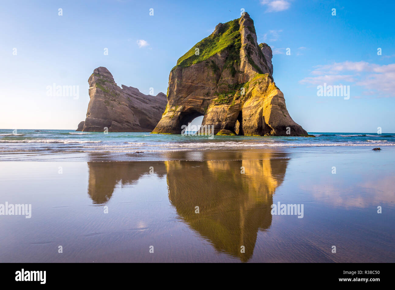 Wharariki Beach, Nuova Zelanda: le splendide formazioni rocciose riflettono in acqua come onde potenti scontro contro la riva. Questo vasto tratto di costa displ Foto Stock