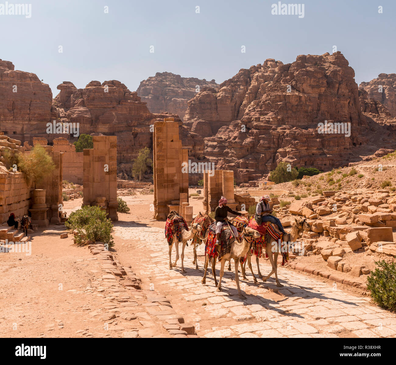 Turistiche e guide su dromedari al Gate Temenos, centro di Petra, antica strada romana accanto alle rovine di Petra Foto Stock