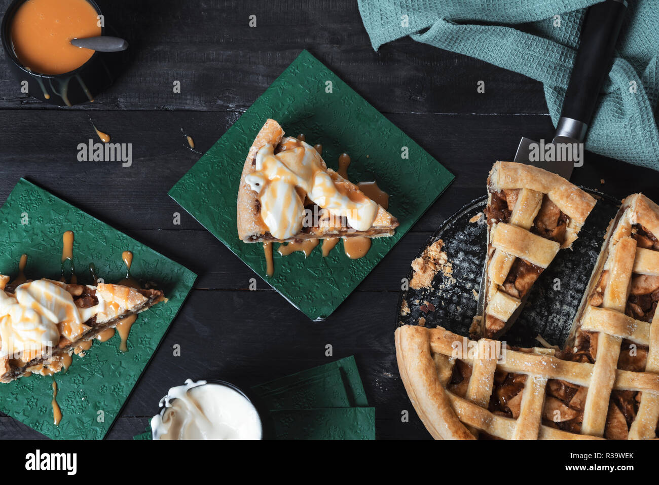 Una deliziosa torta di mele e due fette con panna montata e salsa di caramello, su un nero tavolo rustico. Vista dall'alto. Dessert fatti in casa. Dolce tentazione. Foto Stock