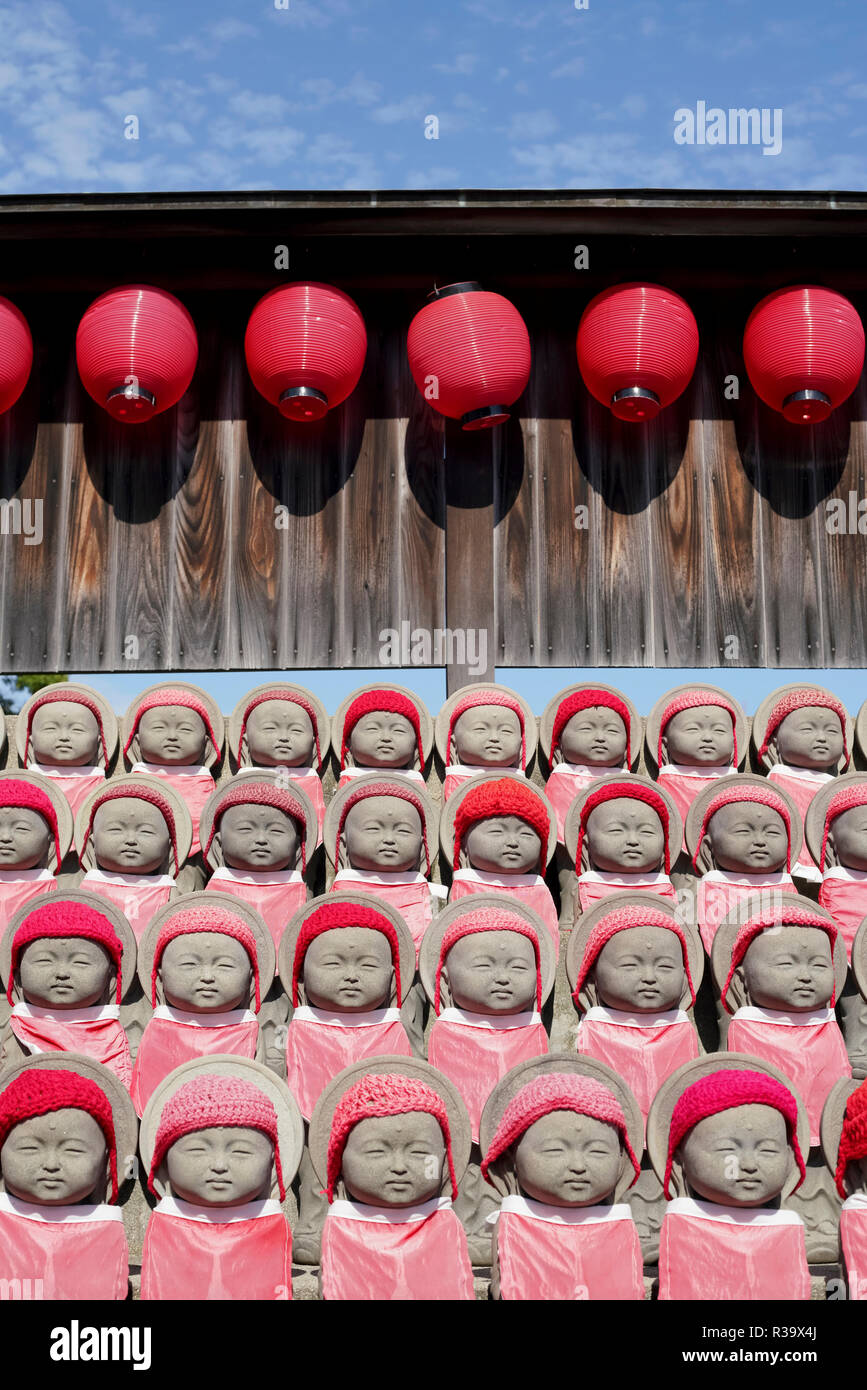 Fila di mizuko buddista jizo statue con red bib, cappello, sciarpa Foto Stock