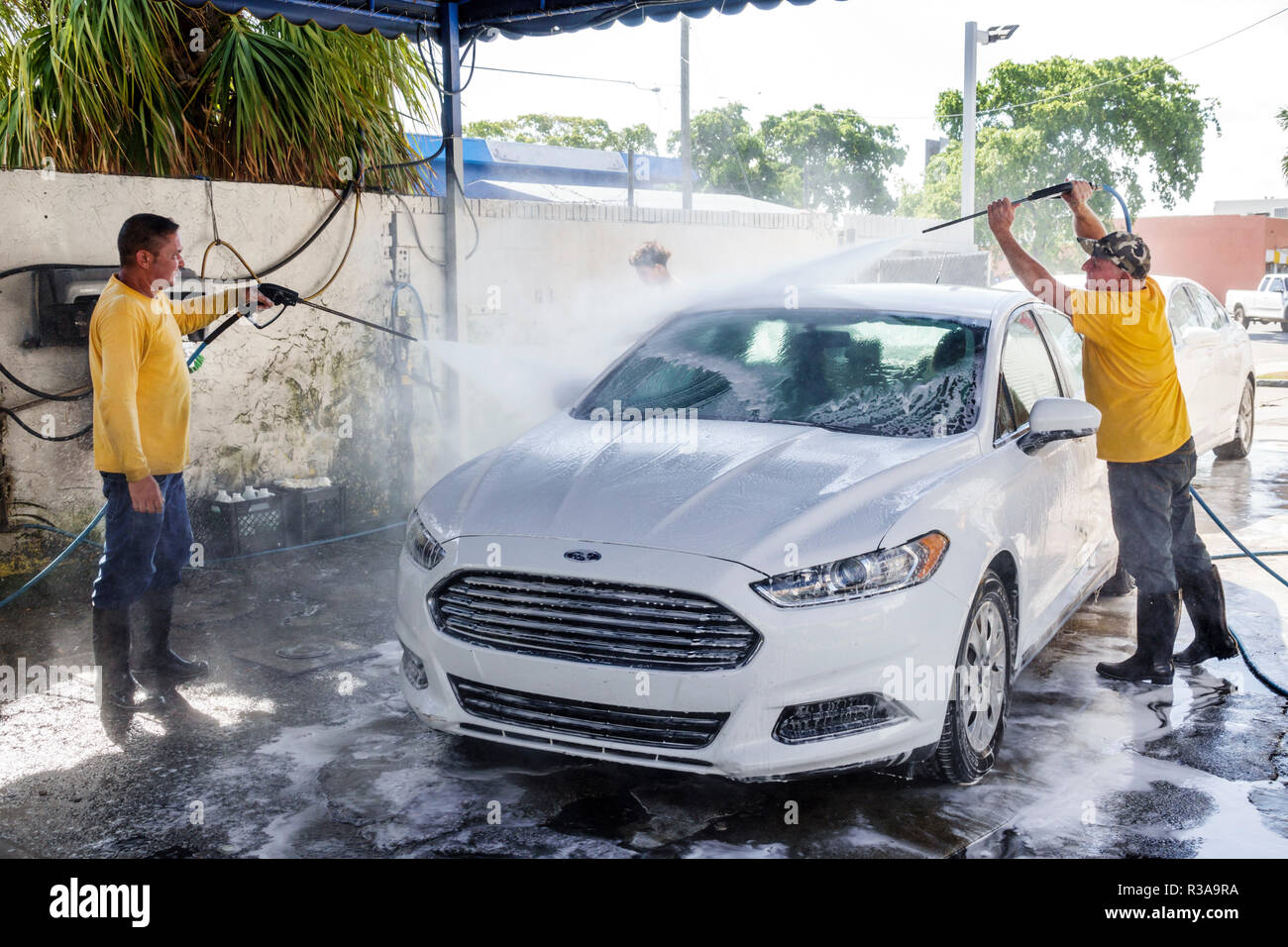 Miami Florida,Little Havana,car wash,bianco Ford Fusion,uomo ispanico maschio,lavoro,pulizia,acqua tubo flessibile spray ad alta pressione, lavoro di squadra,FL18111 Foto Stock