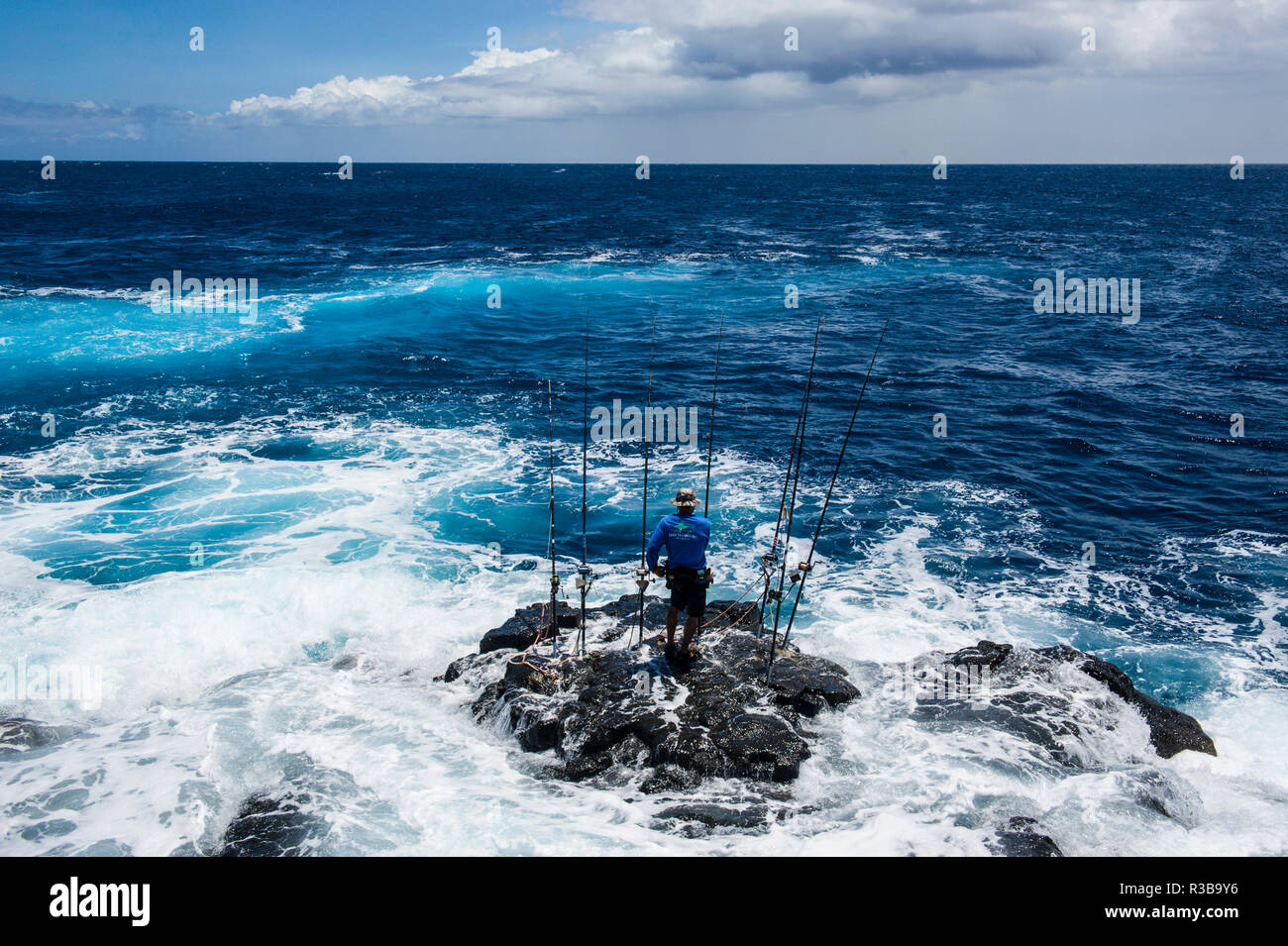 Pescatore in piedi su una roccia nel mare con la sua angolazione aste, Kalae, South Point, Big Island, Hawaii, STATI UNITI D'AMERICA Foto Stock