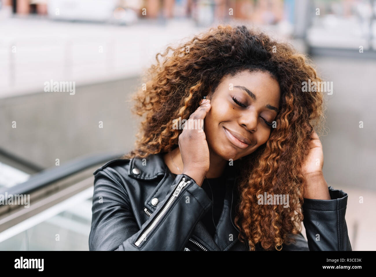 Ritratto di giovane sorridente donna nera indossando giacca di pelle  ascoltando musica in cuffia Foto stock - Alamy