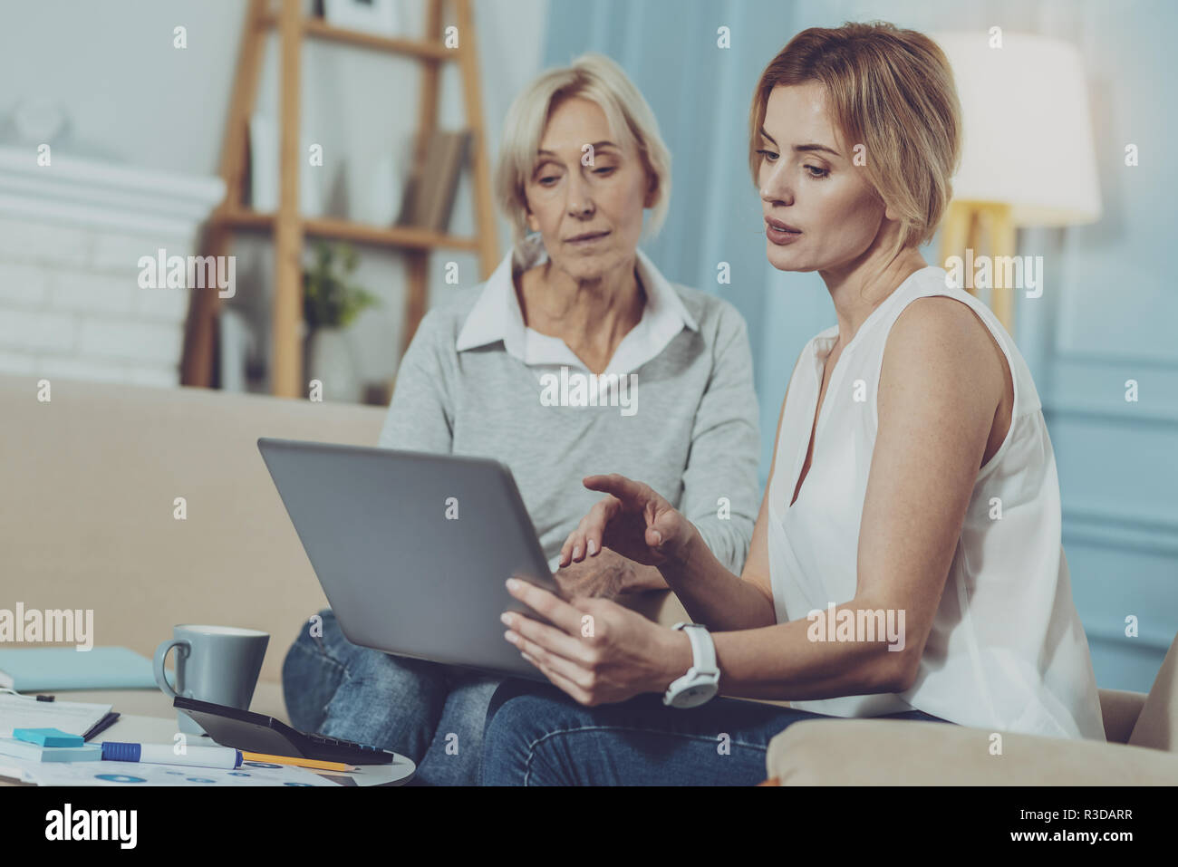 Consultazione. Giovane professionista consulente finanziario seduto vicino a gravi di età compresa tra donna e discutere questioni di lavoro mentre puntare il dito sullo schermo del notebook Foto Stock