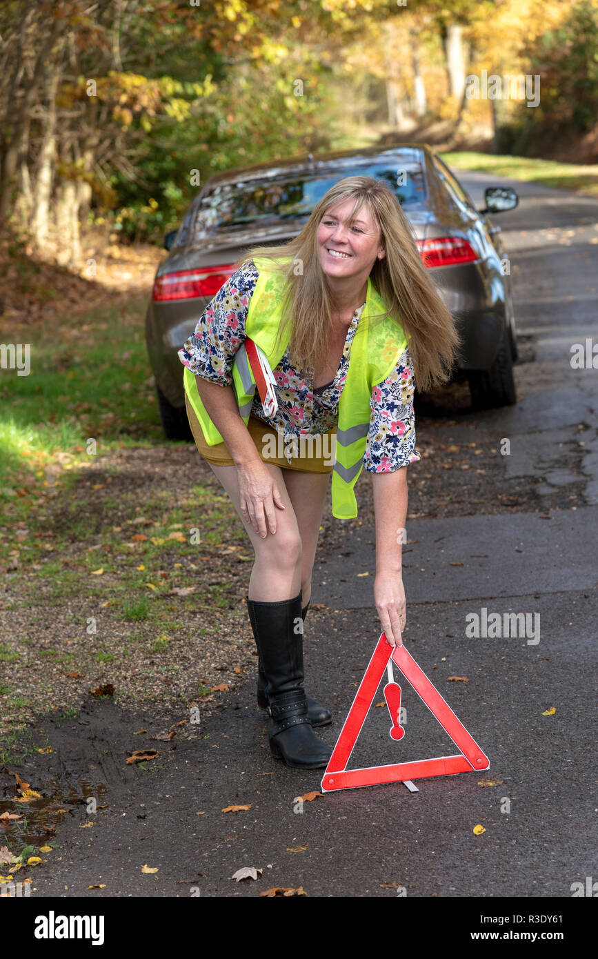 Driver donna mettendo una sicurezza riflettente di un triangolo di avvertimento sul lato posteriore di una macchina Foto Stock