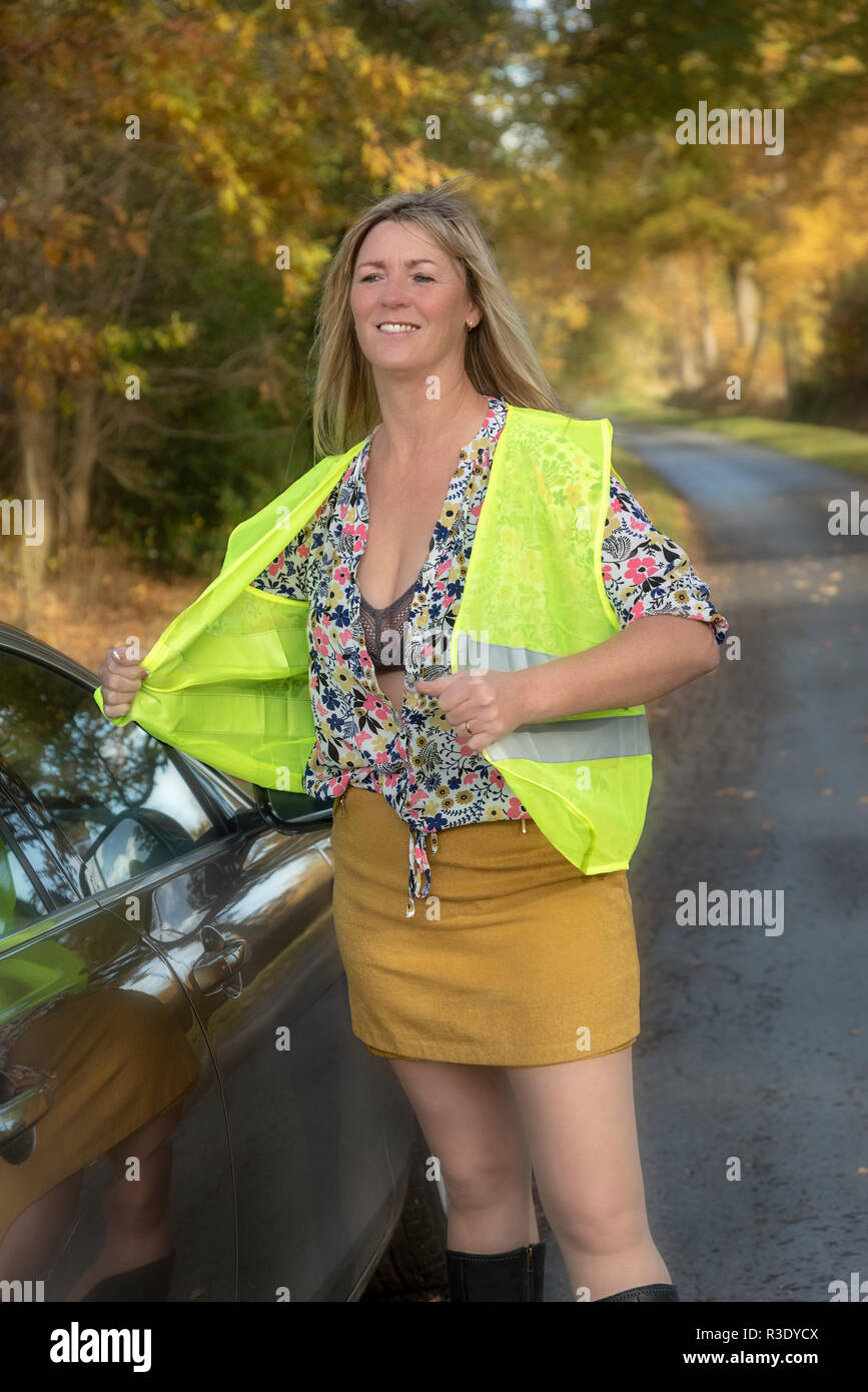 Automobilista femminile mettendo su una riflettente giubbotto di sicurezza su strada Foto Stock