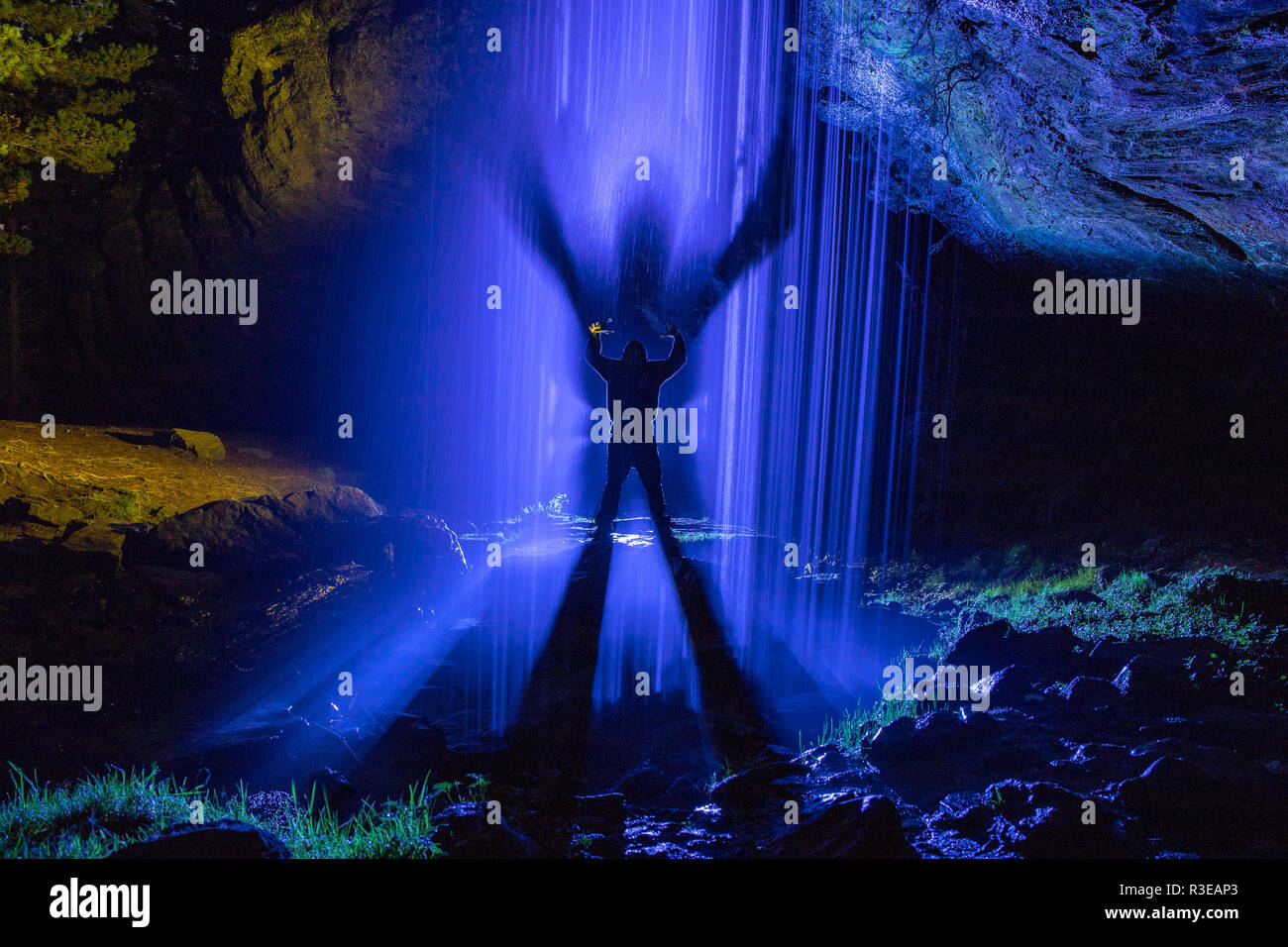 La fotografia notturna all'interno di una grotta con cascata e illuminato con lampioncini colorati per evidenziare la figura del modello. Foto Stock