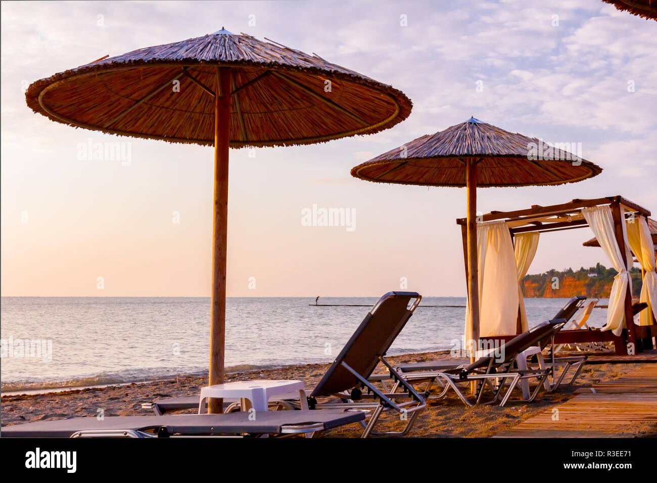 Vista in mattina presto Sun, dawn, sulla spiaggia pubblica con ombrelloni di paglia, ombrelloni e sedie a sdraio lungo la costa del mare. Foto Stock