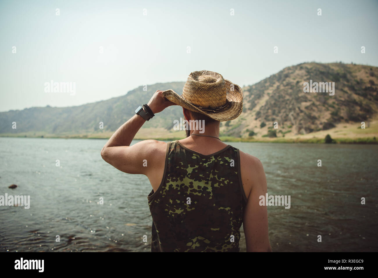 Foto candida di un uomo in cappello da cowboy che guarda il fiume e gode della vista. Faccia in non visibile. Foto Stock