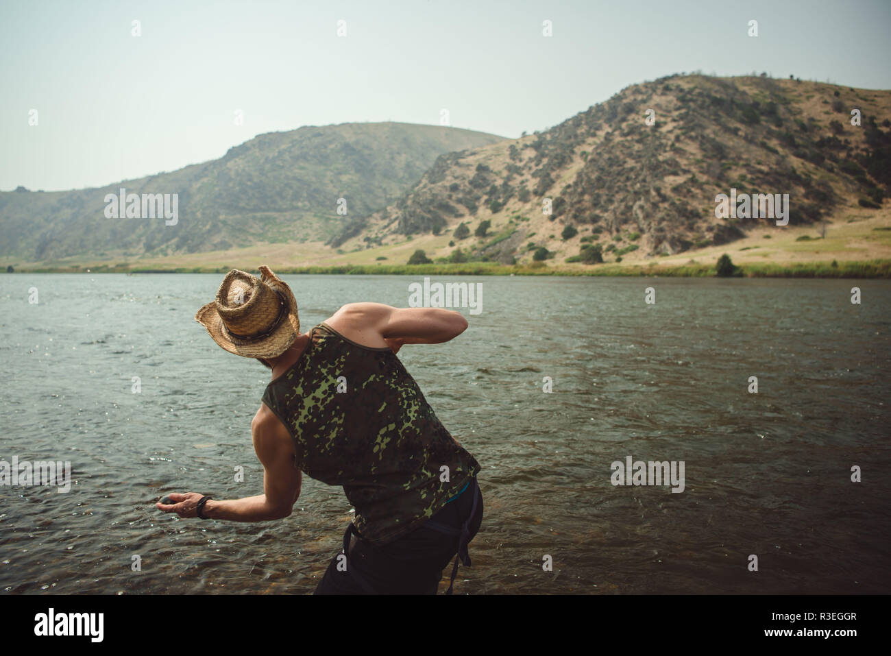Candid fotografia di un uomo in un cappello di cowboy, saltando pietre attraverso il fiume come egli prende una pausa dalla guida sul suo viaggio per allungare le gambe. Foto Stock