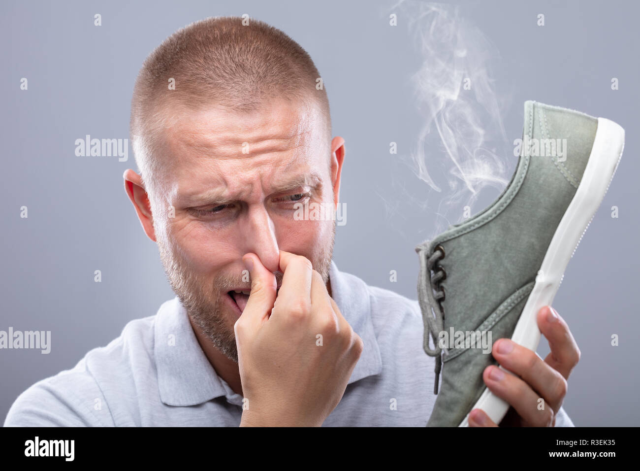Close-up di un uomo che copre il suo naso tenendo Stinky scarpa su sfondo grigio Foto Stock