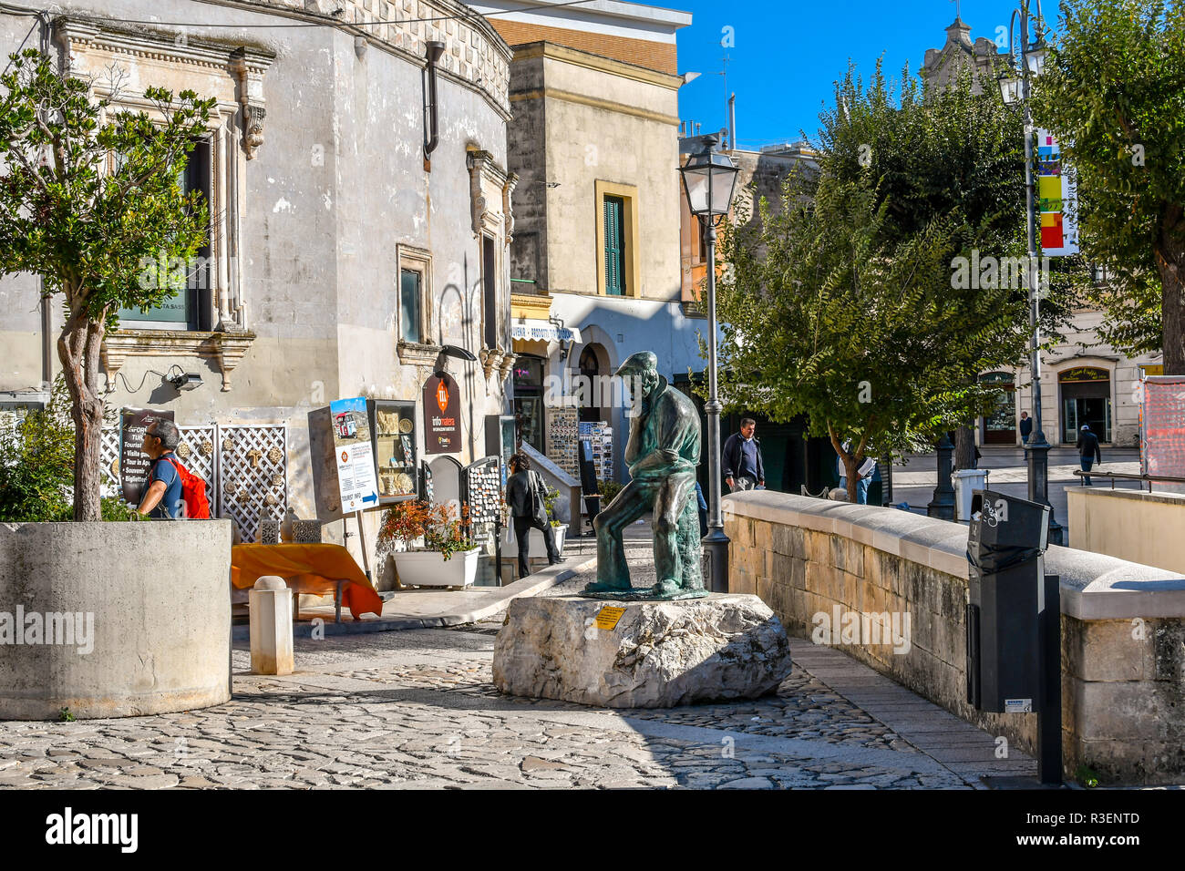Le persone passano in negozi di souvenir vicino alla statua di bronzo di un uomo di pensiero nella Piazza Vittorio Veneto di Matera, Italia, nella regione Basilicata Foto Stock