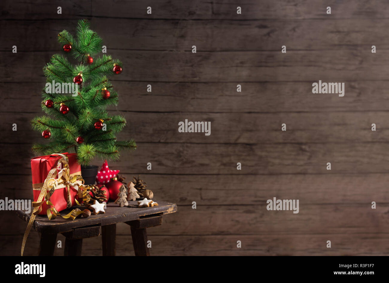 Albero di Natale artificiale con red baubles confezione regalo e decorazione su un piccolo tavolo di fronte un rustico di pareti in legno, generoso spazio di copia selezionato, Foto Stock