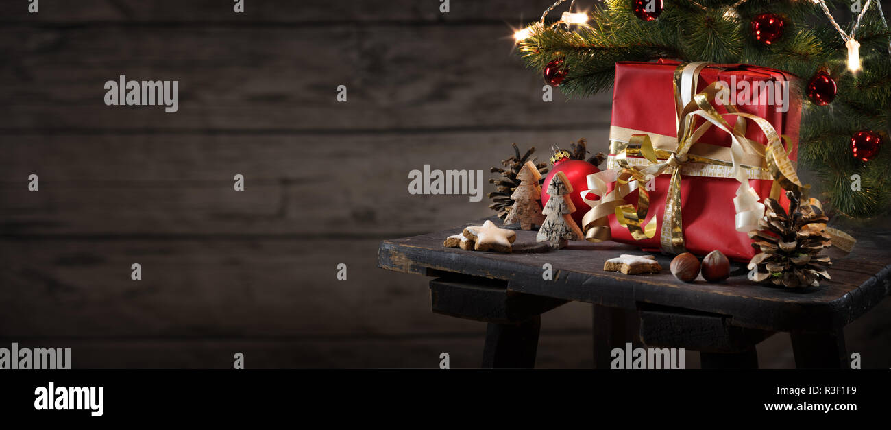 Natale rosso confezione regalo e decorazione su un piccolo tavolo contro un rustico di parete in legno con copia spazio, formato panoramico , messa a fuoco selezionata Foto Stock