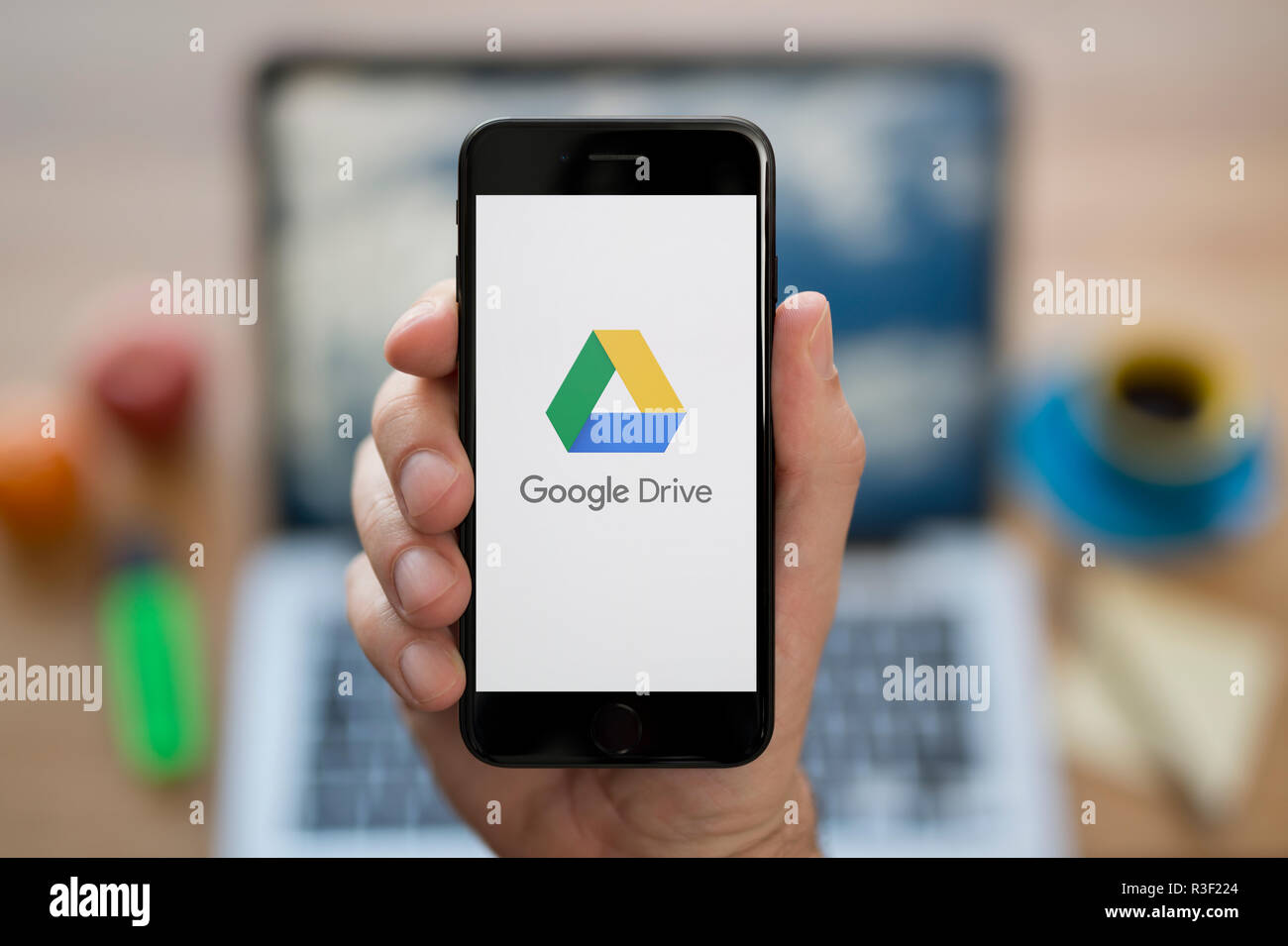 Un uomo guarda al suo iPhone che visualizza le unità di Google logo, mentre se ne sta seduto alla sua scrivania per computer (solo uso editoriale). Foto Stock