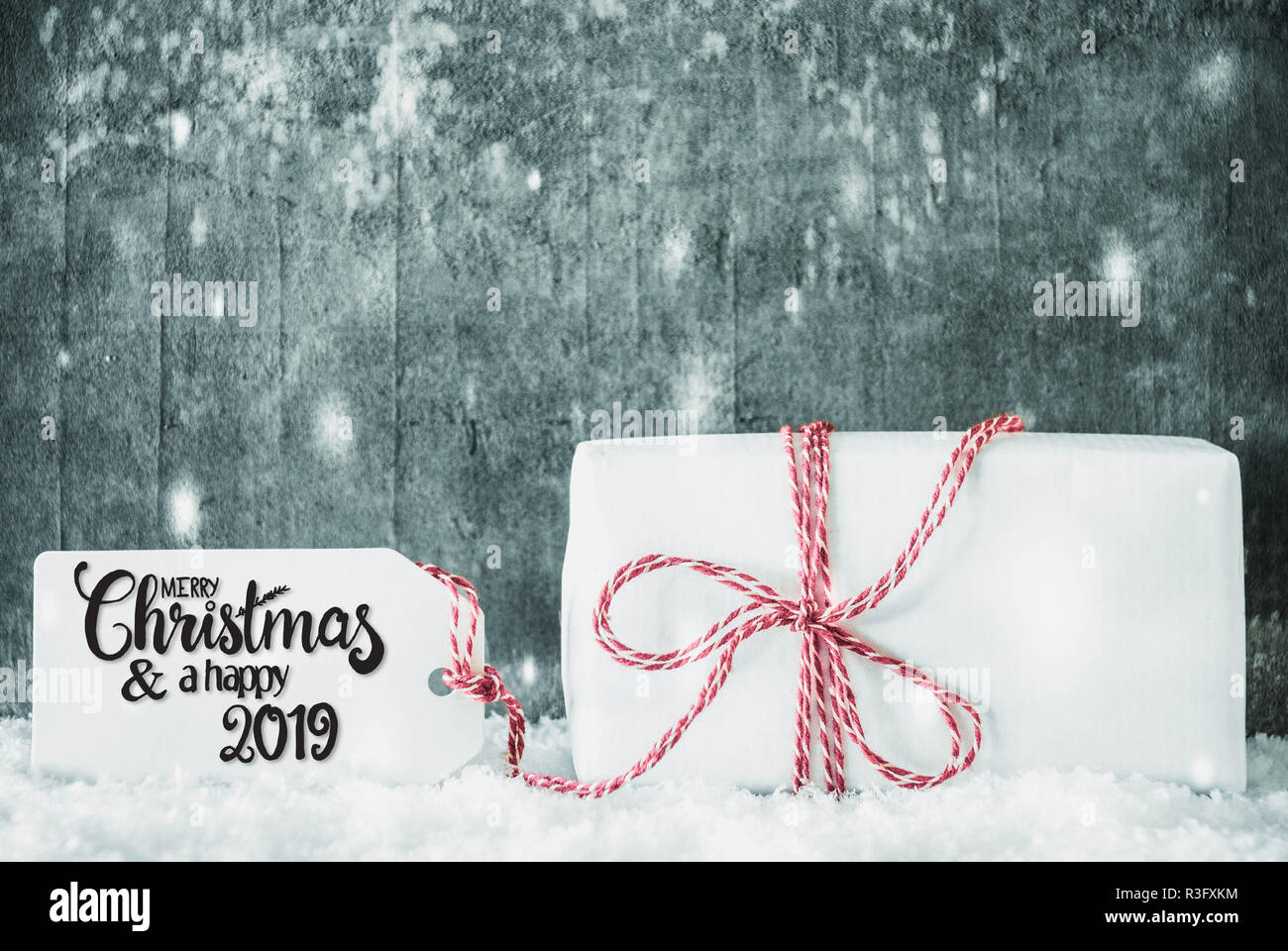 Etichetta con la calligrafia inglese Buon Natale e un felice 2019. Un regalo di bianco con Rosso Ribbn. Grungy sfondo di cemento con la neve Foto Stock