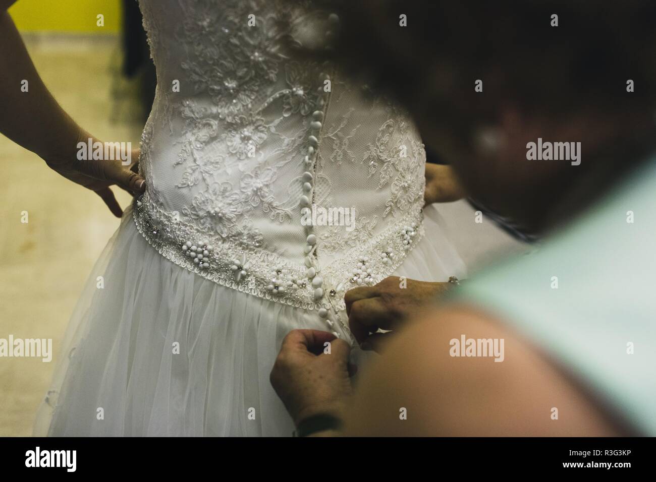 Sposa ottenere pronto, aiutano a lei da abbottonatura i pulsanti sul retro del suo vestito. Foto Stock