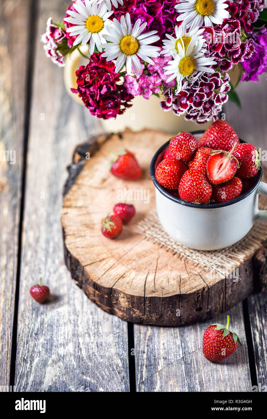 Fragola nel bicchiere vicino a bouquet di fiori sul tavolo di legno Foto Stock