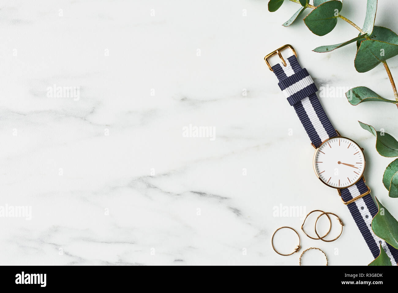 Donna guarda con blu scuro e bianco cinturino in nylon, anelli d oro e eucalipto su marmo bianco dello sfondo. Vista da sopra con copia spazio per il testo. Foto Stock