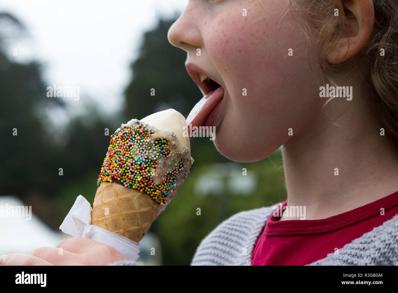 Sei-anno-vecchia ragazza/bambino/kid lambisce un cono gelato e decorate con le centinaia e le migliaia, mentre è fondere rapidamente. (98) Foto Stock