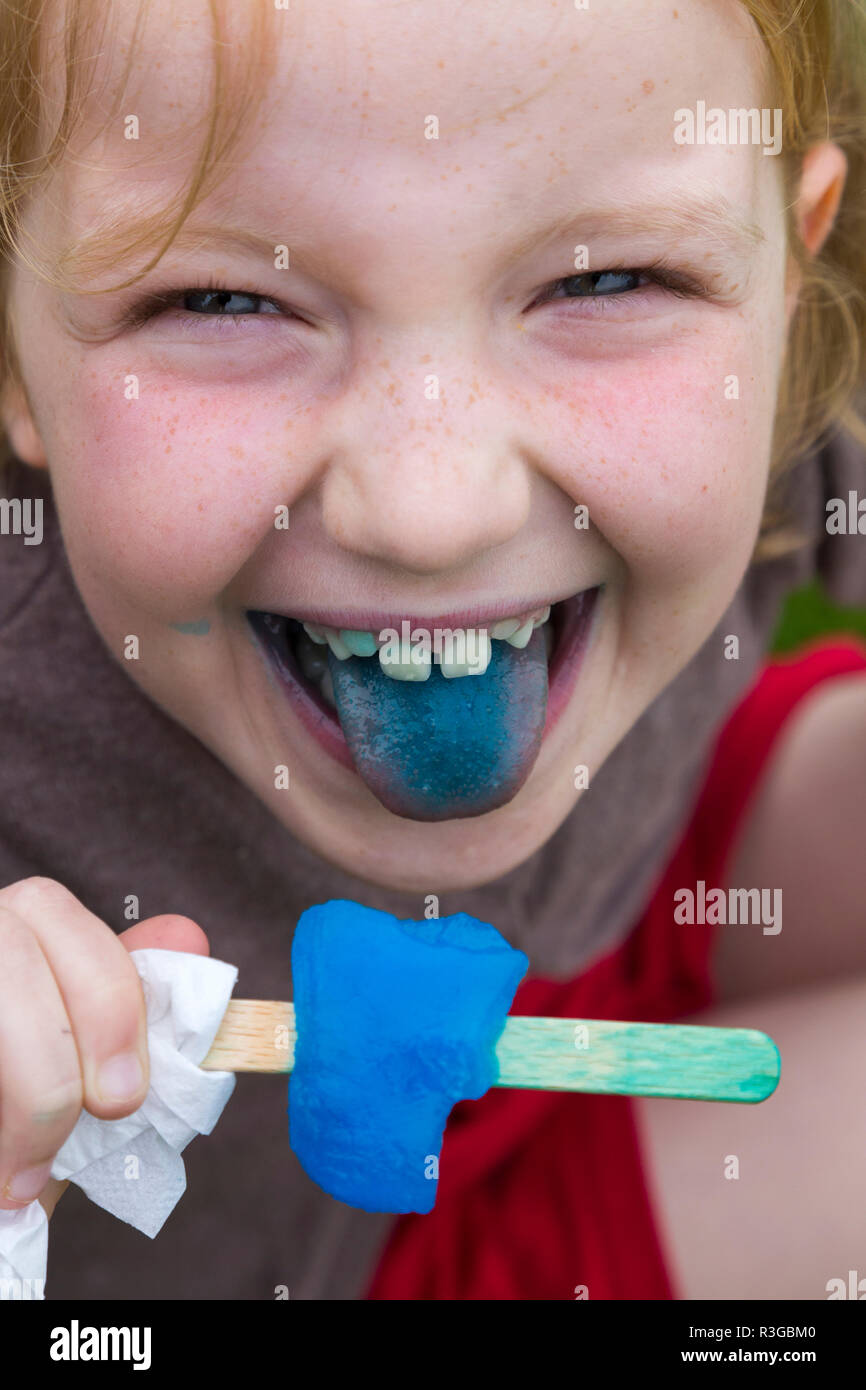 8 anno vecchia ragazza mangiare / leccare un blue ice lollipop / pop per lecca-lecca che la colorazione è la sua lingua e denti blu. UK (98) Foto Stock