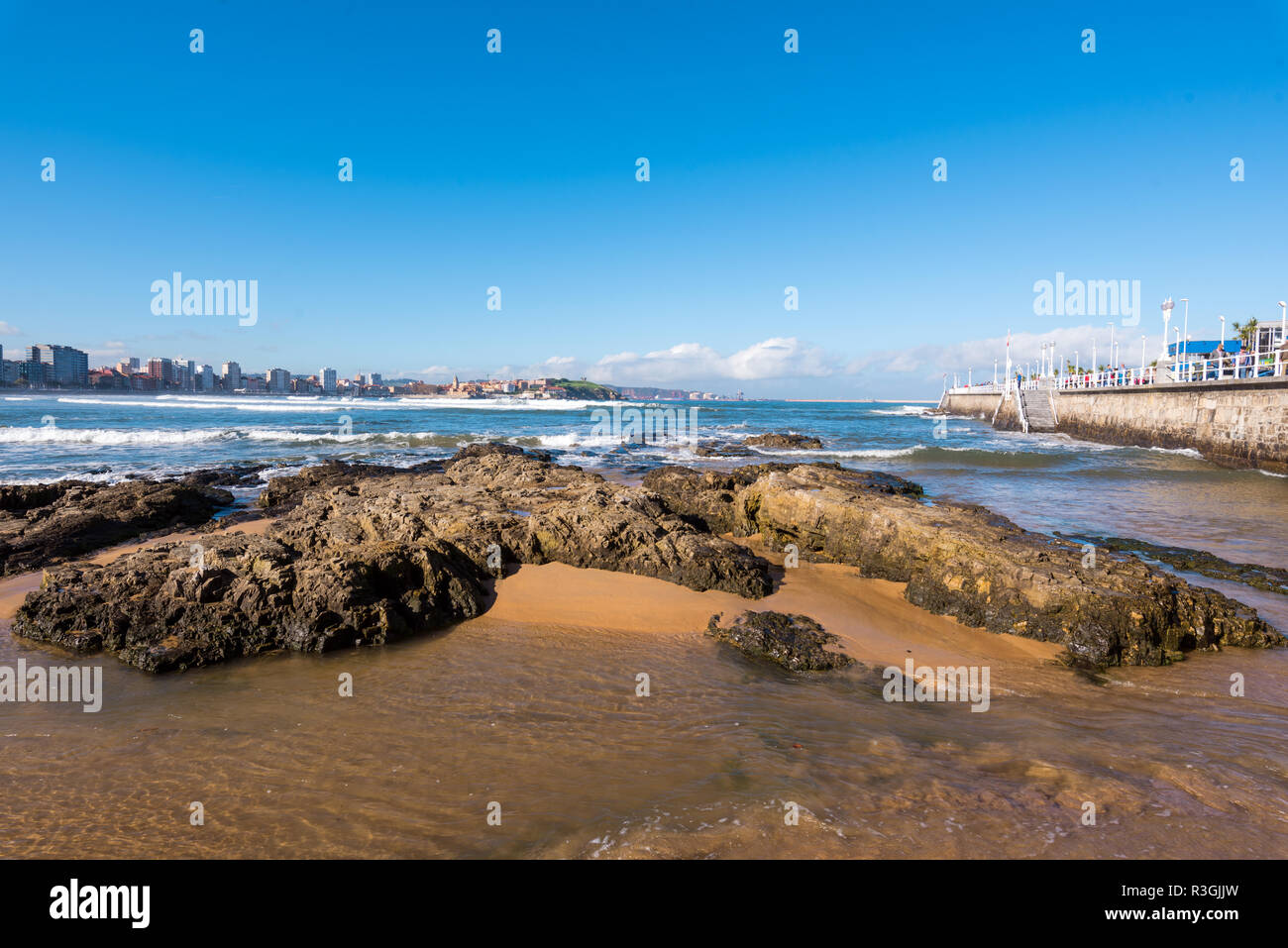 Gijon, Spagna - 19 Novembre 2018: Spiaggia di San Lorenzo e il turista a camminare su una passeggiata in una giornata di sole Foto Stock