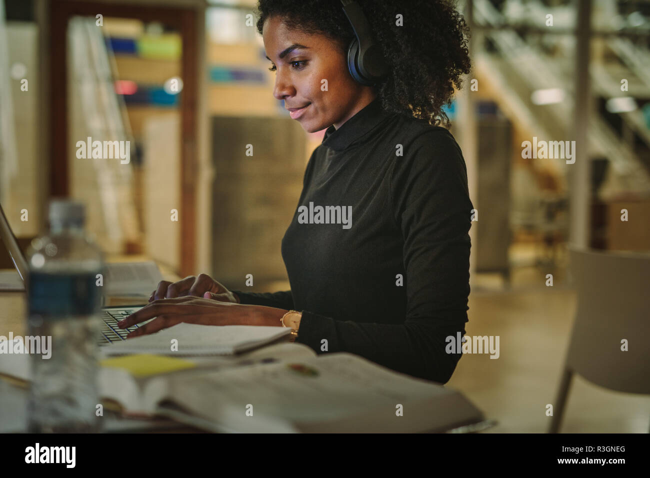 Giovane americano africano ragazza seduta in libreria nella ricerca di informazioni sui notebook per la sua assegnazione. Giovane donna seduta a tavola navigando in internet per n Foto Stock