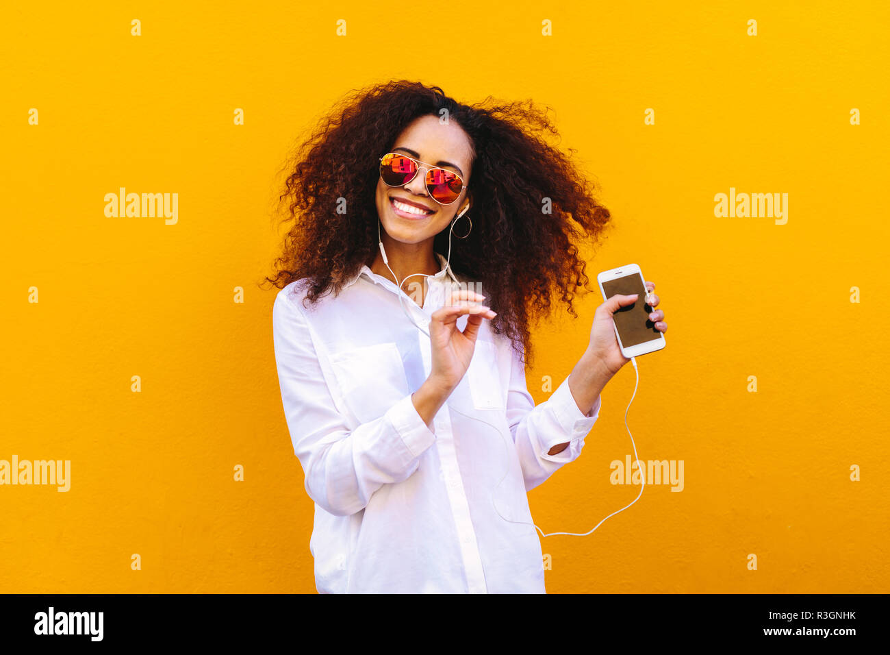 Bella giovane donna ascoltando la musica dal suo telefono e balli. Ragazza africana ascoltando musica e ballando contro la parete gialla. Foto Stock