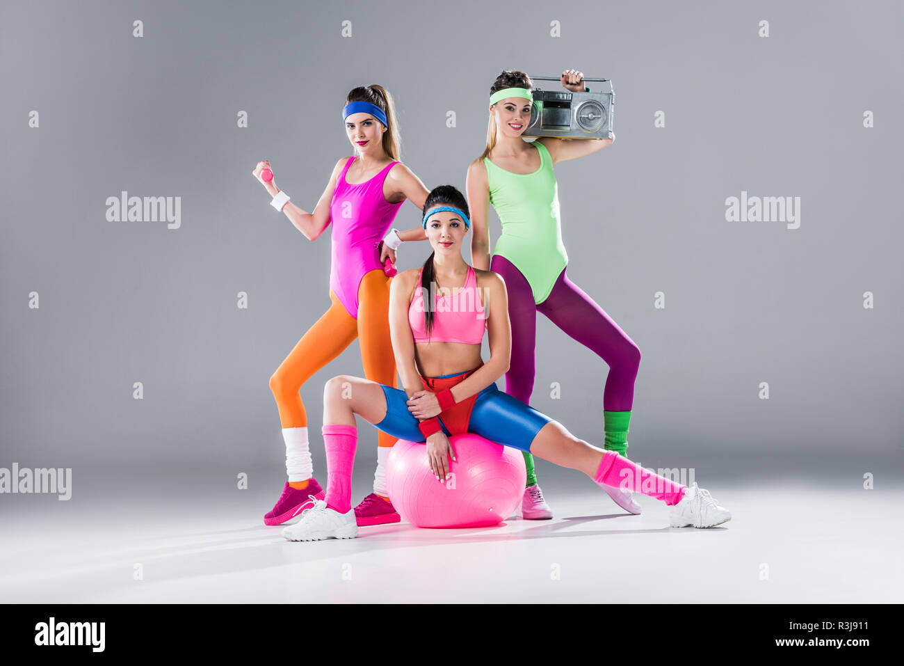 Felice ragazze sportivo con attrezzature sportive e registratore a nastro su grigio Foto Stock