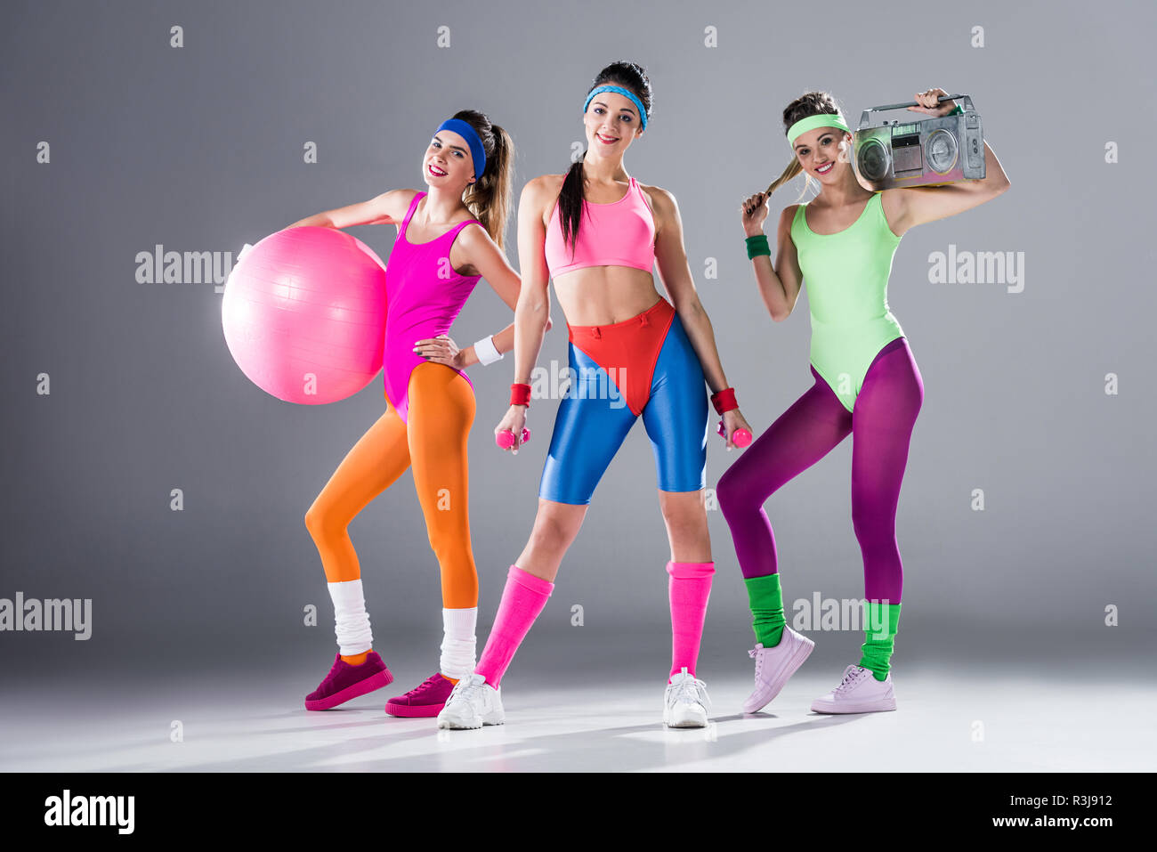 Belle ragazze sportivo con attrezzature sportive e registratore a nastro sorridente in telecamera su grigio Foto Stock