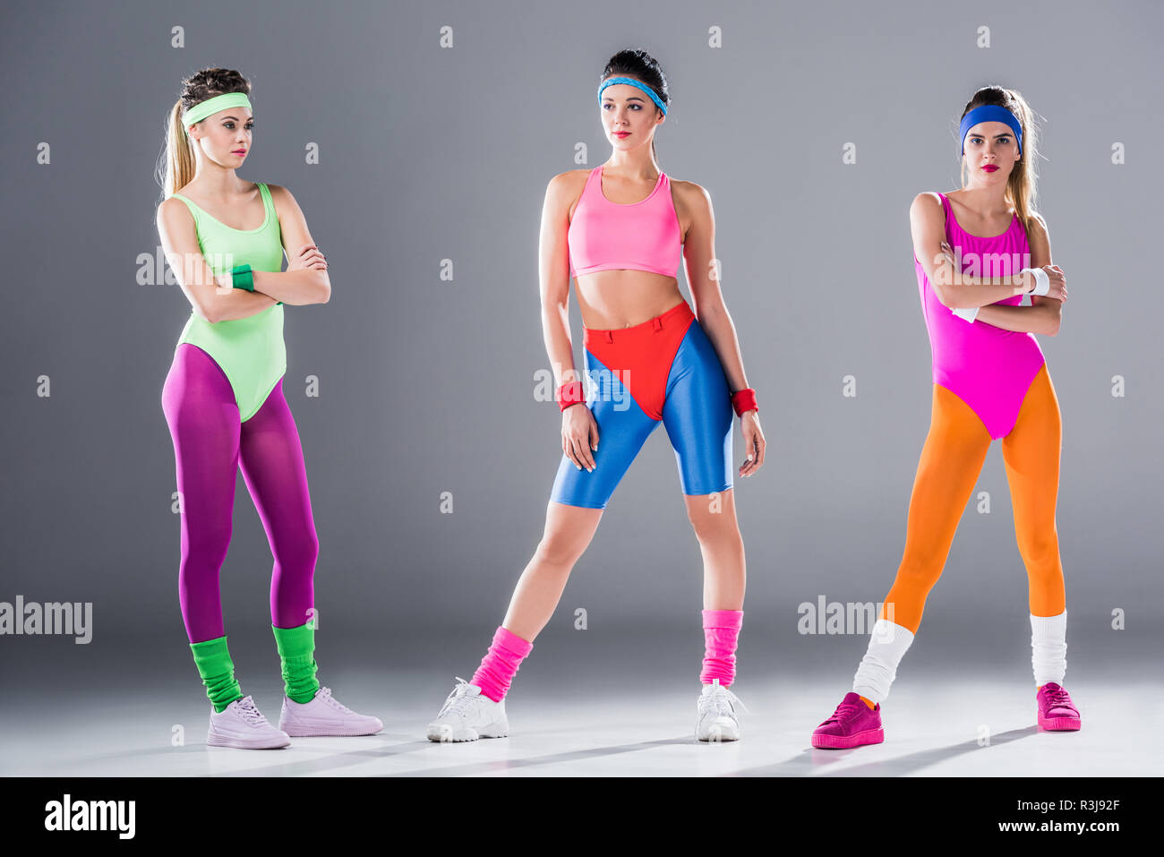 Lunghezza piena vista atletico di giovani donne in 80s style sportswear in posa su grigio Foto Stock