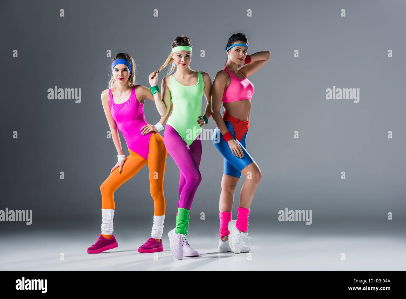 Attraente ragazze sportivo in 80s style sportswear in posa insieme e guardando la telecamera su grigio Foto Stock