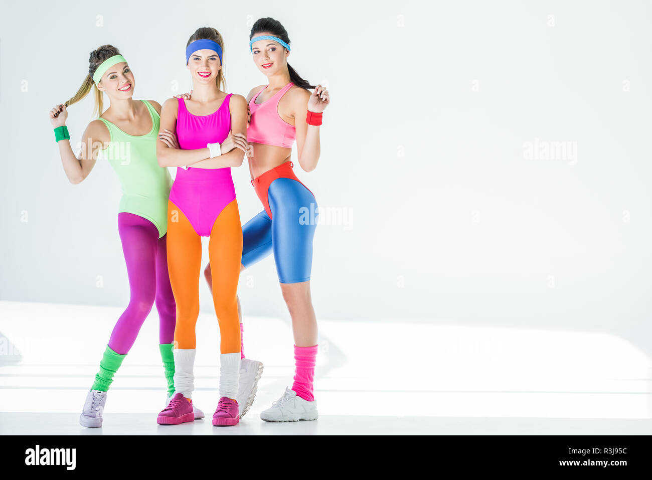 Lunghezza piena vista di belle ragazze atletiche in 80s style sportswear sorridente in telecamera su grigio Foto Stock