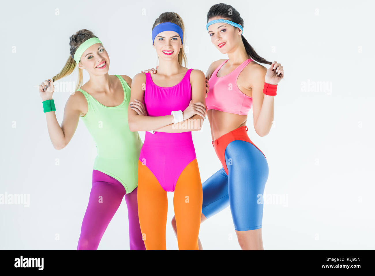 Belle ragazze atletiche in 80s style sportswear sorridente in telecamera isolato su grigio Foto Stock