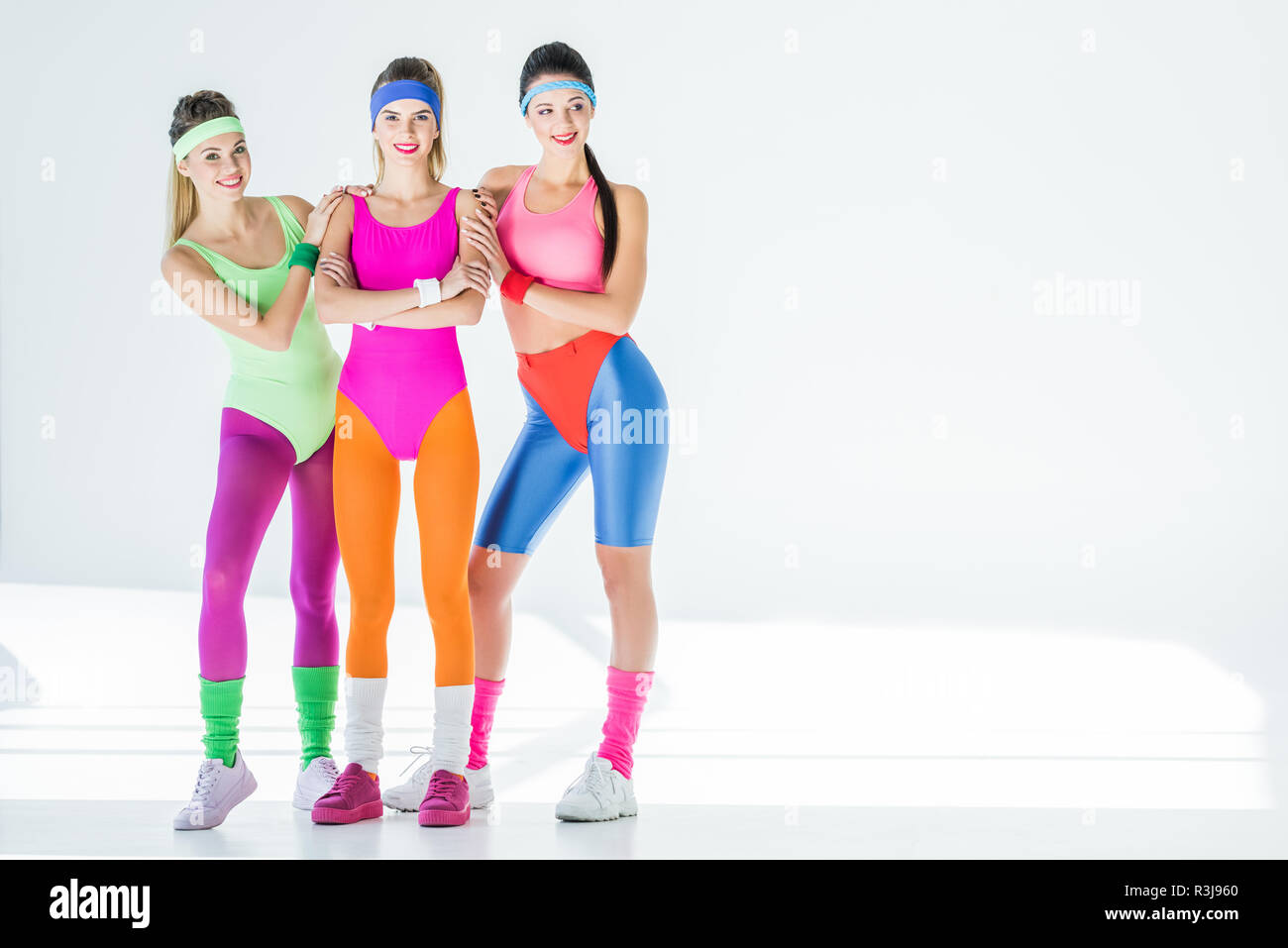 Bella sportiva delle giovani donne in 80s style sportswear sorridente in telecamera su grigio Foto Stock