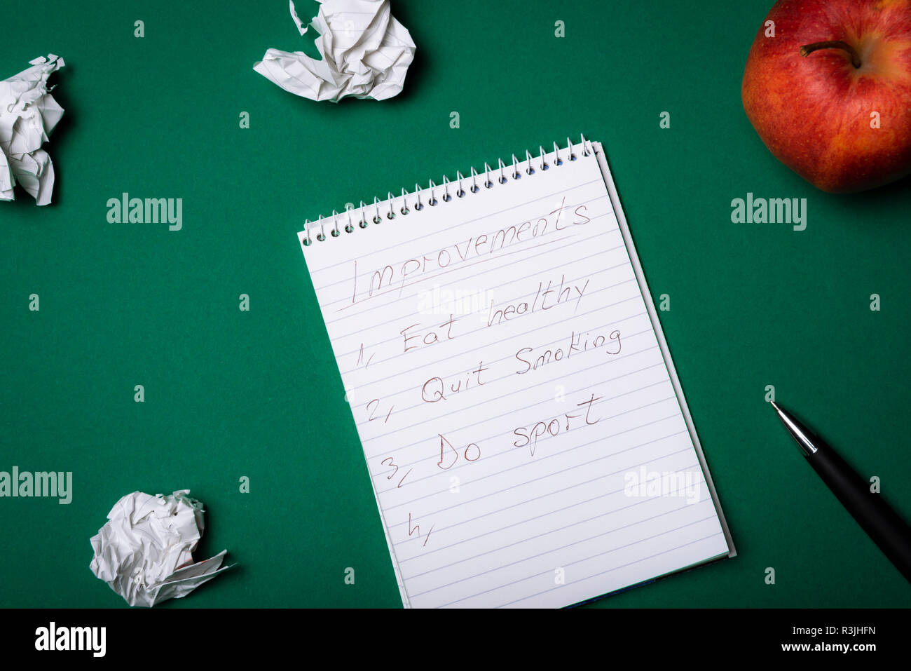 Notebook a spirale con un elenco dei miglioramenti, mangiare sano, smettere di fumare, fare sport, e accartocciata pagine e un apple. Vista dall'alto. Risoluzioni. Foto Stock